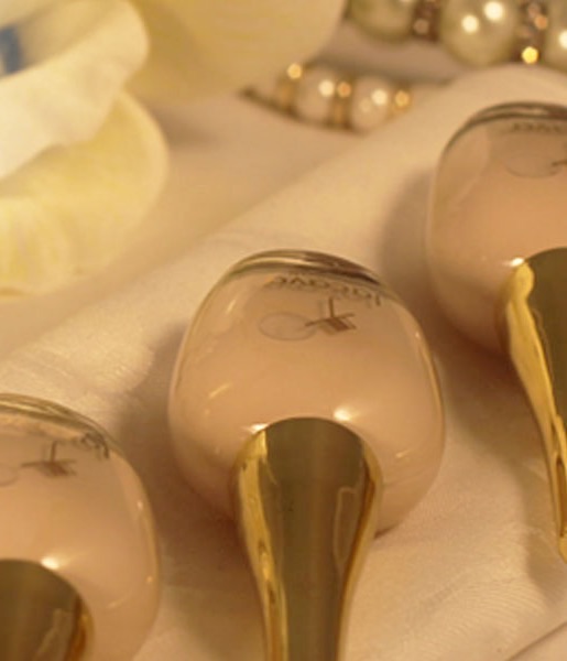 JACAVA London nail polish bottles with gold caps resting on cream silk beside pearls.